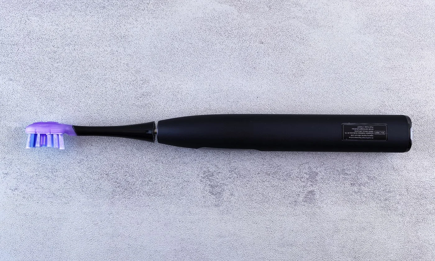 Black electric toothbrush with purple bristles on a textured gray surface