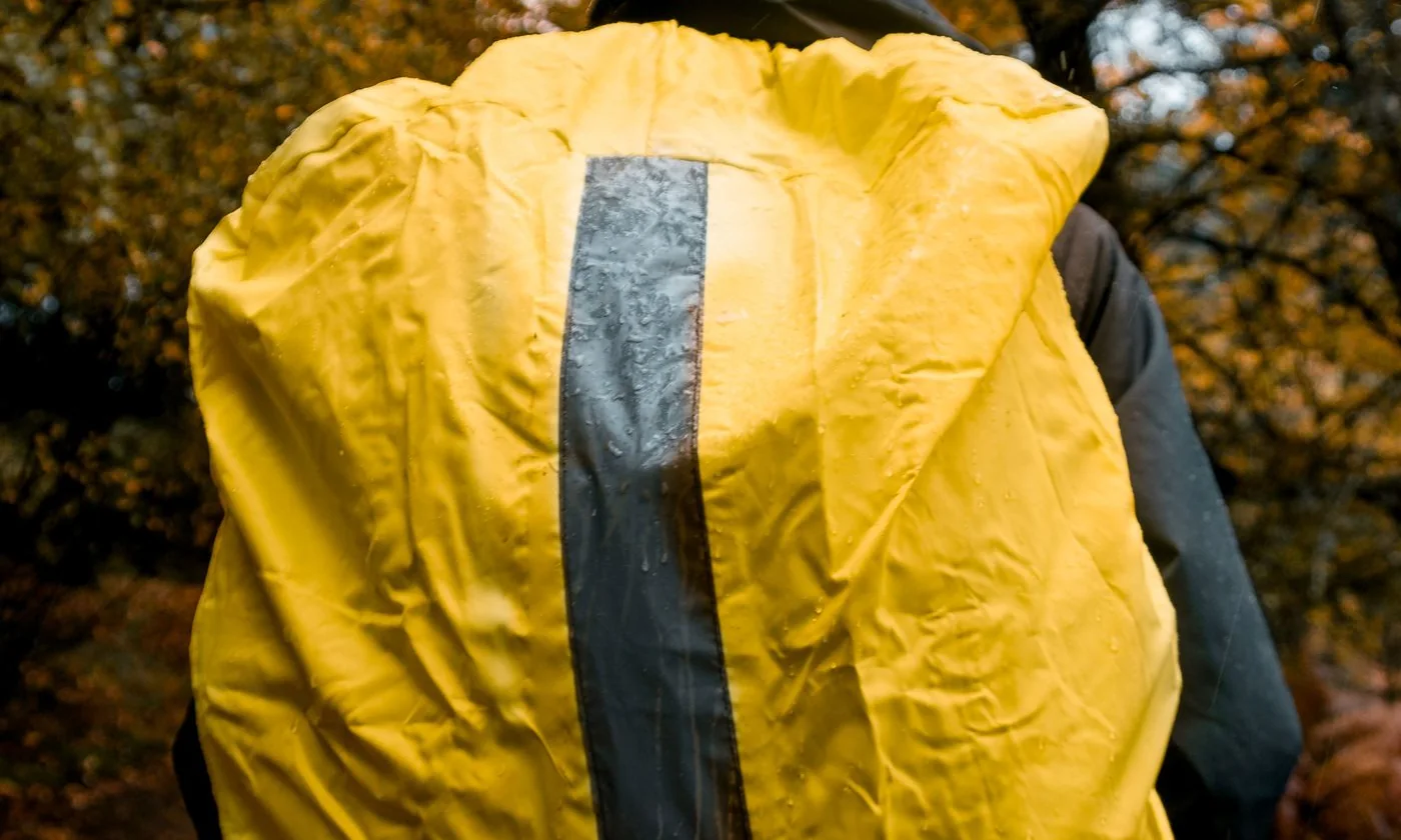 Hiker carrying a yellow backpack along an autumn forest trail