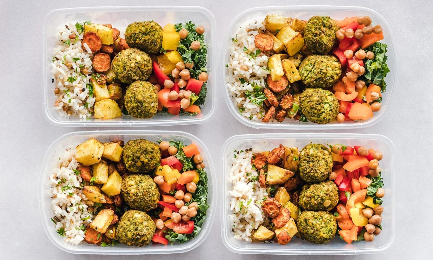 Meal prep containers filled with vegetables, grains, and falafel