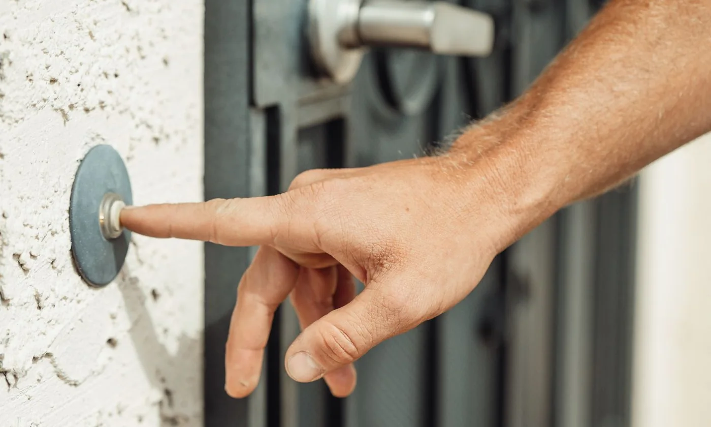 A hand pressing a doorbell beside a residential entrance
