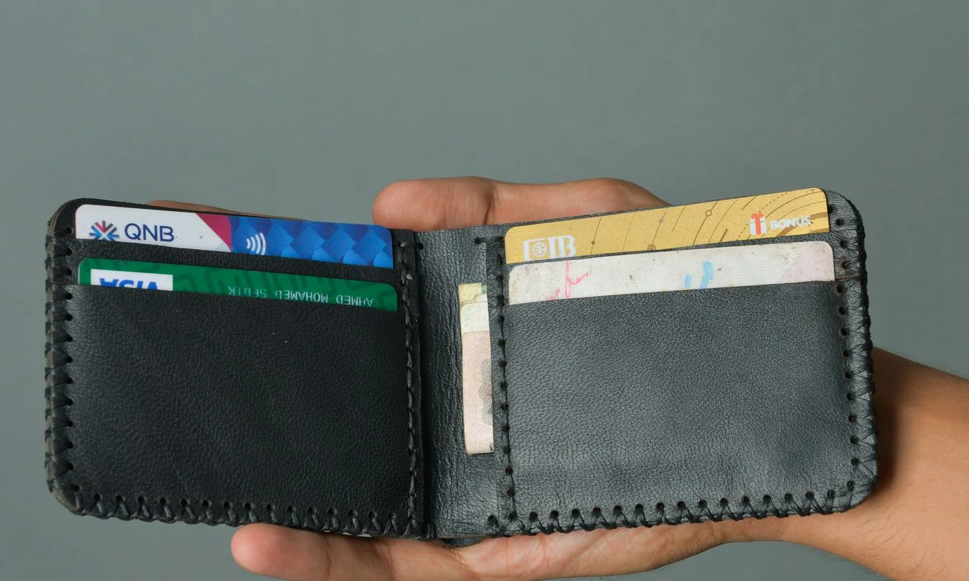 Hand holding a black wallet containing cards